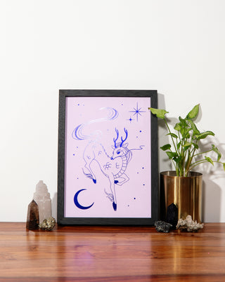 A framed art print on a wooden table with crystals and pot plant.