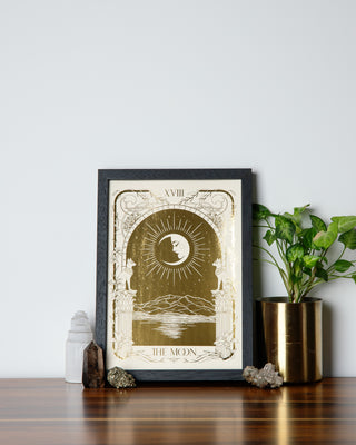 A framed gold art print surrounded with crystals and pot plant on a wooden table.