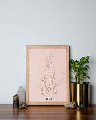 Framed artwork labeled libra on a wooden surface with several crystals and a potted plant nearby