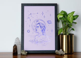Framed artwork of a Aquarius woman with celestial elements on a table with decorative items.