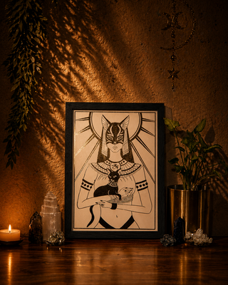 Framed artwork of a cat goddess on a wooden surface with candles and plants.