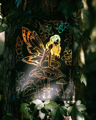 Decorative pixie art print sitting on a mushroom in a forest setting