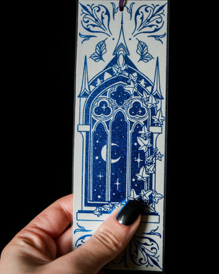 Decorative cathedral bookmark with blue and grey design held by a hand against a black background
