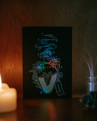 A mini A6 black card featuring a glowing neon-style illustration of a potion bottle, displayed on a dark surface next to a lit candle.