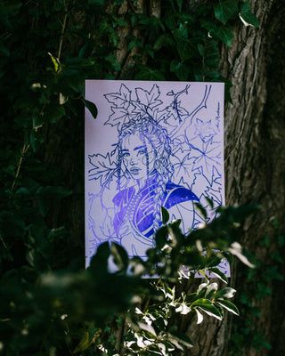 Indigo foil print of a fairy with floral elements on a white card, placed against a tree trunk.