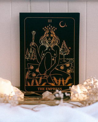 Tarot card featuring 'The Empress' on a wooden surface with candles and crystals.