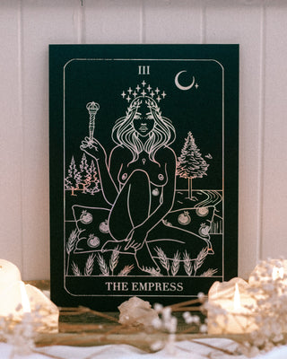 Tarot card featuring 'The Empress' with candles and crystals on a wooden surface.