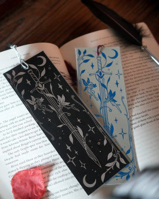 Two decorative bookmarks on an open book with a feather pen and red flower.