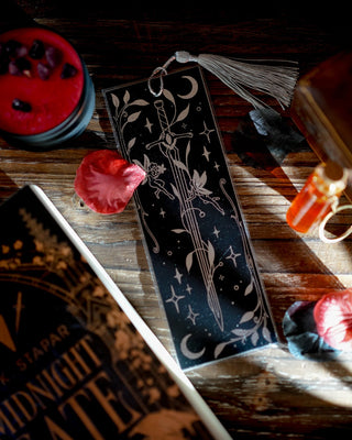 Fae sword bookmark on a wooden surface with a candle and rose petals