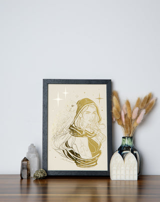 An art print featuring a maiden with a golden hue and an owl on her shoulder, surrounded by feathers and a twilight glow, displayed in a black frame.