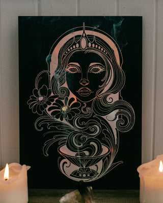 Decorative wall art with a stylized face design on a black background, flanked by two lit candles.