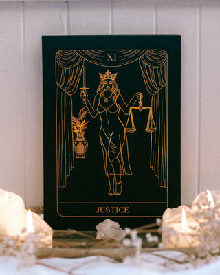 Decorative tarot card with 'Justice' symbol on a table with candles and crystals.