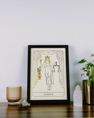 Framed tarot card print titled 'Justice' on a table with decorative items.