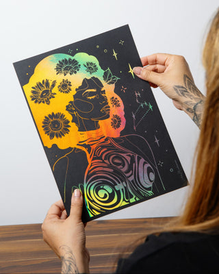 A person holds up a black art print featuring holographic gold foil, stylized portrait of a Leo woman with stars on a plain background
