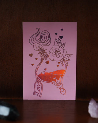 Pink card with red love potion design featuring a rose, hearts, and the word 'Love' on a dark brown background.