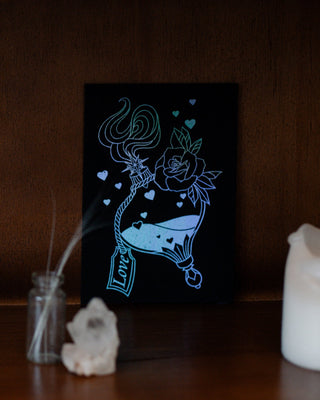 Silver mini A6 print of a love potion on a wooden shelf.