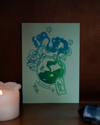 Green mini  card with luck potion design next to a lit candle on a wooden surface