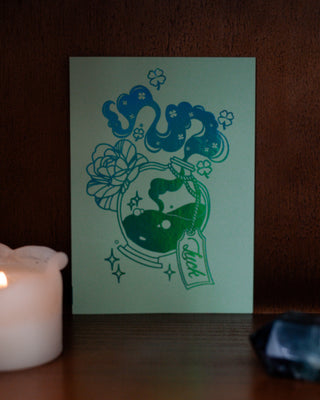 Green card of luck potion design next to a lit candle on a wooden surface