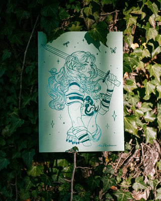 A vertical art print featuring a stylized teal line drawing of a fairy with a sword, displayed outdoors against a background of green ivy.