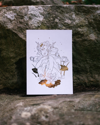 An art print featuring a delicate line drawing of a nymph surrounded by lotus flowers, with metallic gold foil accents, displayed against a textured gray stone background.