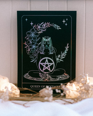 Tarot card with a pentacle design and 'Queen of Pentacles' text, surrounded by candles on a white surface.