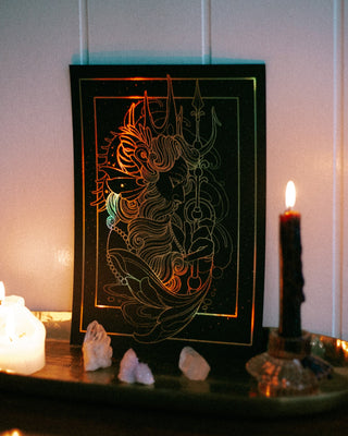 A black art print featuring Poseidon art illustration in metallic gold and copper tones, displayed on a shelf with lit candles and crystals against a paneled wall.