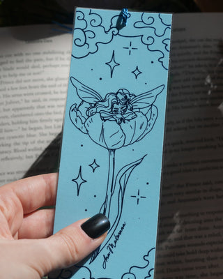 Hand holding a blue bookmark with angel design on an open book