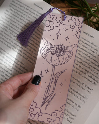 Hand holding a pixie bookmark with floral design on an open book.