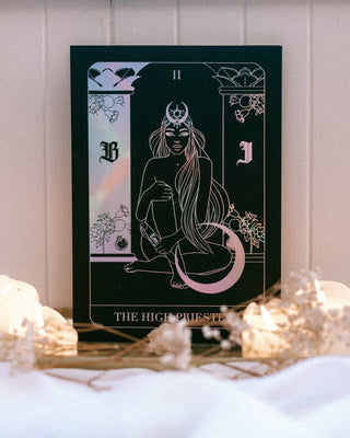 Tarot card featuring 'The High Priestess' with decorative elements on a soft surface.