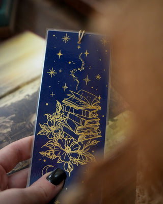 Blue bookmark with gold star and book illustration held by a hand.