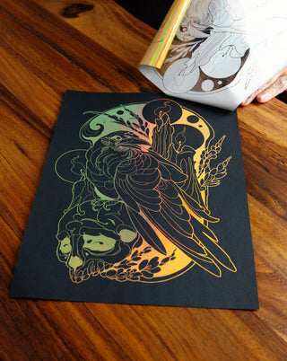 An art print with a bird and skull in gold foil on a table..