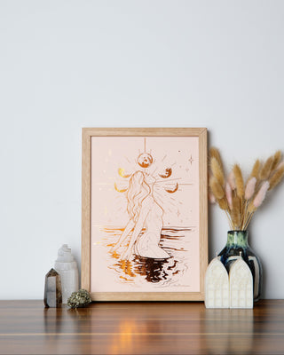 A framed illustration of a female figure with flowing lines that resemble water or steam, set against a light background, placed on a wooden surface with decorative items around it.