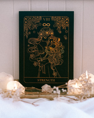 Tarot card titled 'Strength' with candles and crystals on a white surface