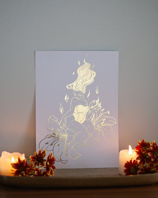 Alessia fire nymph art print in gold foil on white card, flowing hair and flowers, styled with candles and autumn leaves