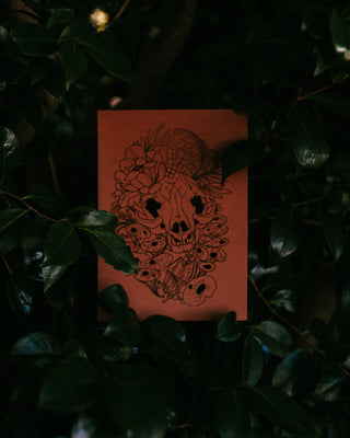 Brown card with black skull design on a dark leafy background