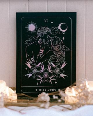 Tarot card titled 'The Lovers' with candles and crystals on a wooden surface.