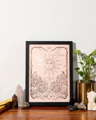 Framed tarot card artwork of 'The Sun' with decorative items on a wooden surface.