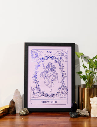 Framed tarot card print titled 'The World' on a wooden surface with decorative items.