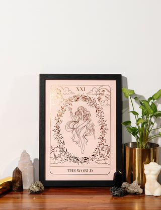 Framed tarot card print titled 'The World' on a wooden surface with decorative items.