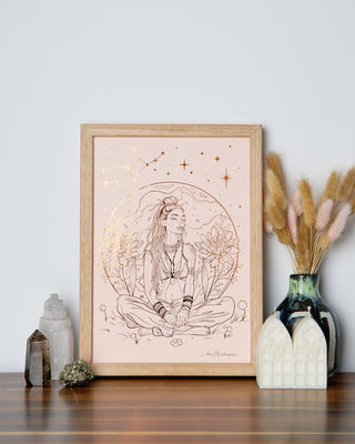 An art print featuring a stylized illustration of a woman surrounded by a circular frame, possibly representing the Virgo sign, with a backdrop of greenery and a subtle use of color. The print is framed in a light wood frame, displayed on a table with decorative items around it.