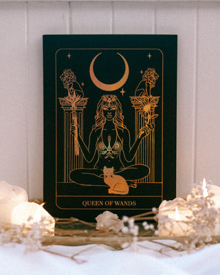 Decorative card titled 'Queen of Wands' with a woman holding a wand and a sunflower on a white surface with candles.