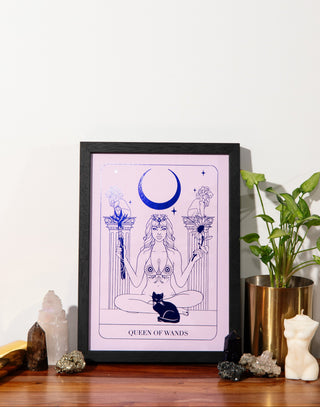 Framed artwork of a woman with a crescent moon on a pink background, surrounded by crystals and plants.