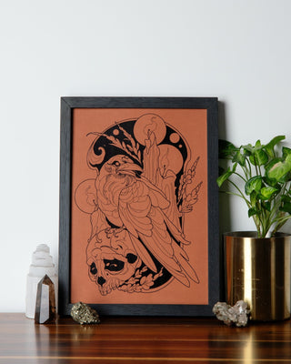 Whispering Shadows raven art print in black foil on brown card, photographed outdoors among dark leaves and branches