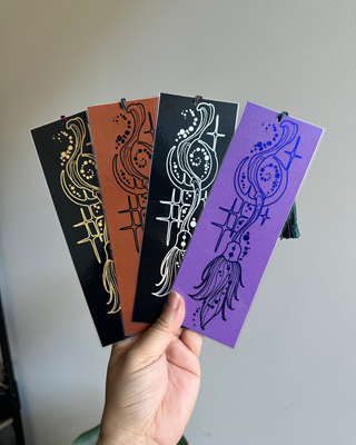 Hand holding four decorative bookmarks with broomstick designs on a plain background