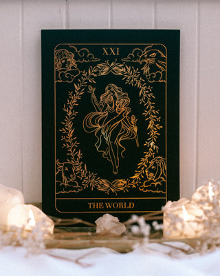 Decorative book titled 'The World' with gold illustrations on a white surface with candles.