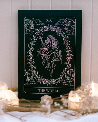 Tarot card titled 'The World' with candles and decorative elements on a white surface.