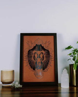 An art print featuring a stingray design, framed in a black frame, displayed on a wooden surface with decorative items around it.