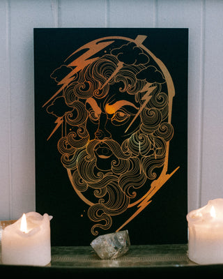 Decorative wall art featuring a Greek god Zeus design on a black background, set against a surface with candles and a crystal.