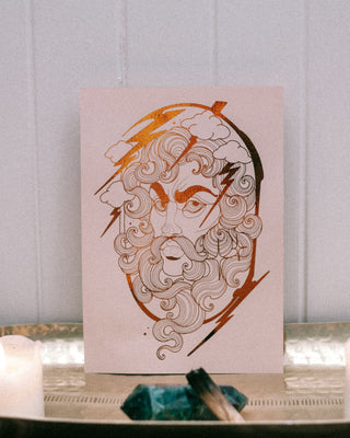 A vertical art print featuring a stylized line drawing of the Greek God Zeus with copper accents, displayed on a silver tray with two lit white candles and crystals against a white paneled wall.