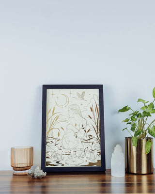 A illustration of a pregnant lady by the pond displayed on a wooden surface with a full moon object and decorative plants beside it.